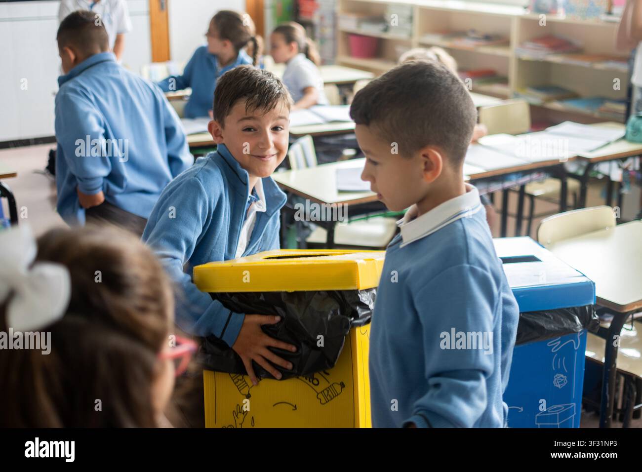 Bambini delle scuole elementari che partecipano al riciclo in classe utilizzando contenitori per il riciclo con codice a colori durante la giornata scolastica. Foto Stock