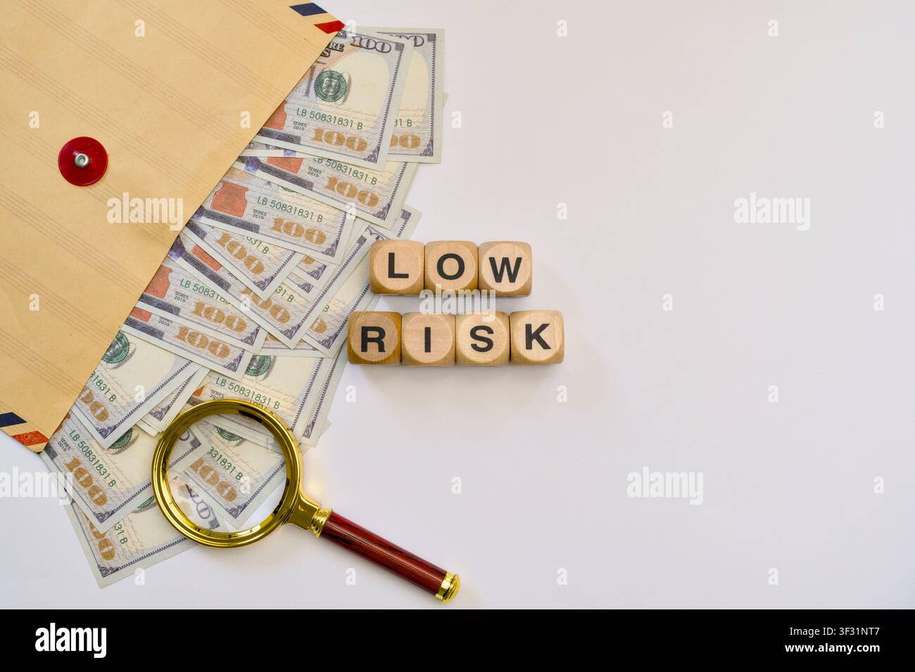 Blocchi di legno che formano la scritta „low risk“ con banconote di dollari statunitensi e una lente d'ingrandimento su sfondo bianco. Foto Stock