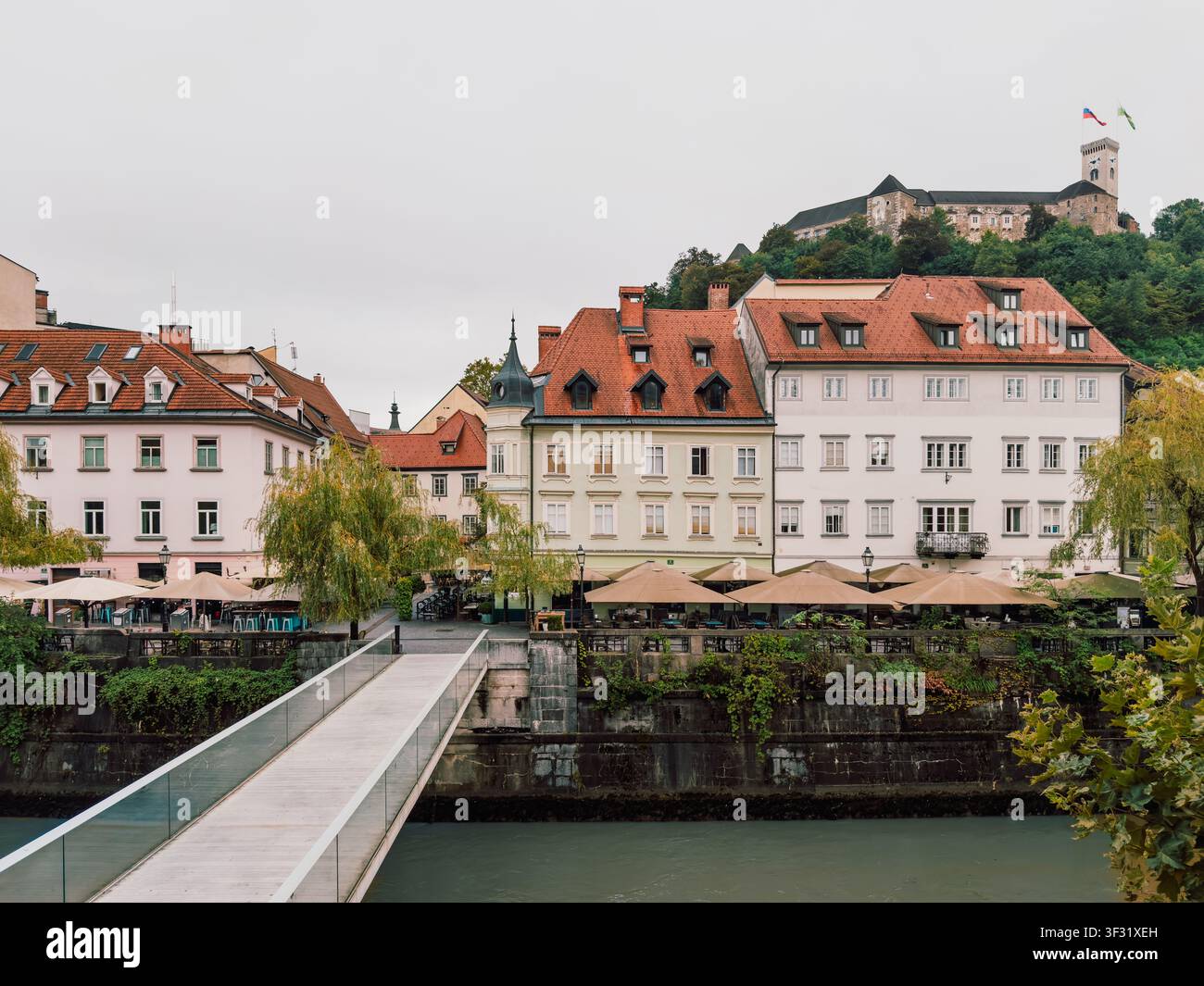 Vista del castello di Lubiana che si erge sopra il centro storico e il fiume Ljubljanica in Slovenia, con edifici colorati e un moderno ponte pedonale Foto Stock