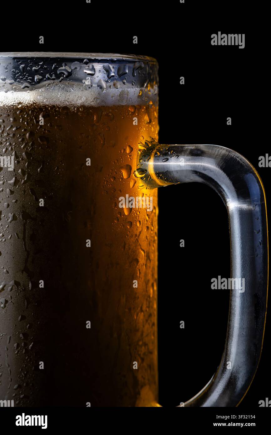 Una tazza di vetro piena di birra mostra gocce d'acqua all'esterno. Lo sfondo è scuro, evidenziando la bevanda. Foto Stock