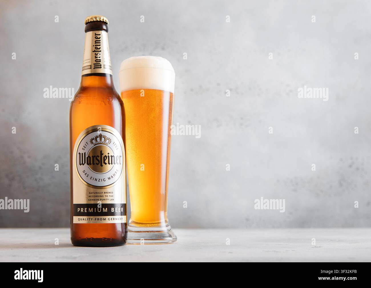 LONDRA, REGNO UNITO - 12 APRILE 2026: Bottiglia e bicchiere di birra bionda Warsteiner su tavolo chiaro. Foto Stock