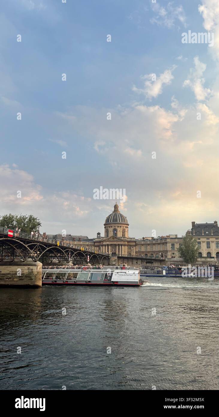 La cupola storica dell'Istitut de France che risplende al tramonto, vista attraverso la Senna con il Pont des Arts e una chiatta fluviale. - Immagine stock catturata con smartphone