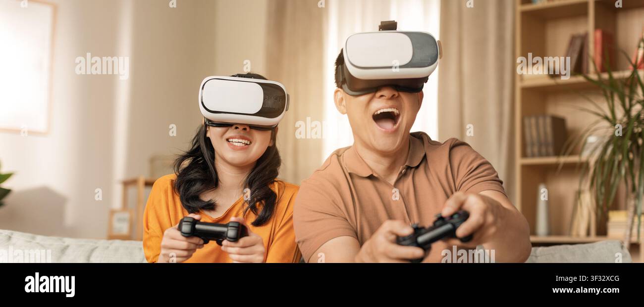 Uomo e donna asiatici felici che giocano ai videogiochi con cuffie VR a casa, atmosfera allegra Foto Stock
