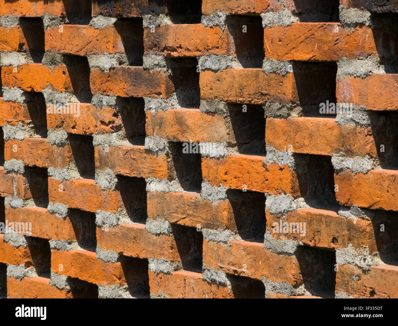 Primo piano di un muro di mattoni rossi con un motivo geometrico di fori di ventilazione aperti e ombre forti. Perfetto per sfondi architettonici. - Immagine stock catturata con smartphone