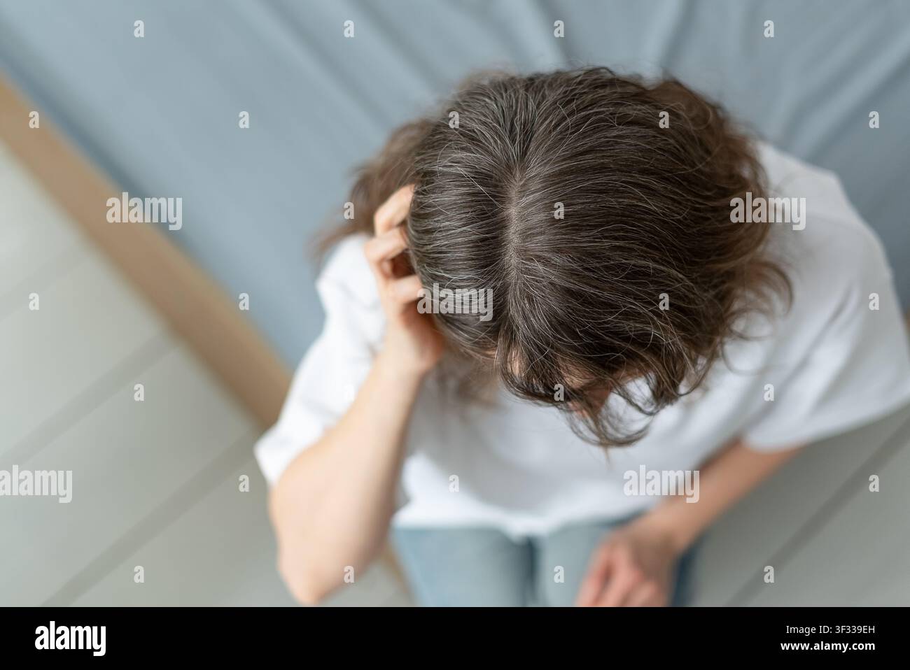 Una donna stima quanto dei suoi capelli sia già diventato grigio. L'adulta matura calcola la percentuale di ciocche argentate rispetto al colore naturale. La madre misura la sua progressione di invecchiamento. Foto Stock