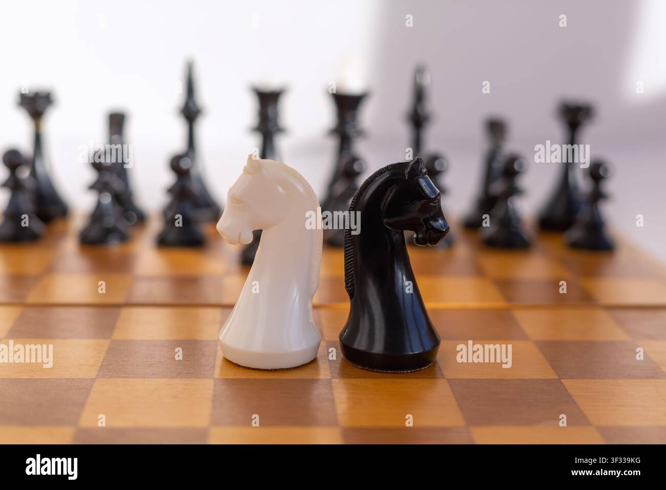 Cavalliere di scacchi bianchi e neri su una classica scacchiera di legno con pezzi sfocati sullo sfondo. Simbolo di strategia, rivalità e competizione intellettuale f Foto Stock