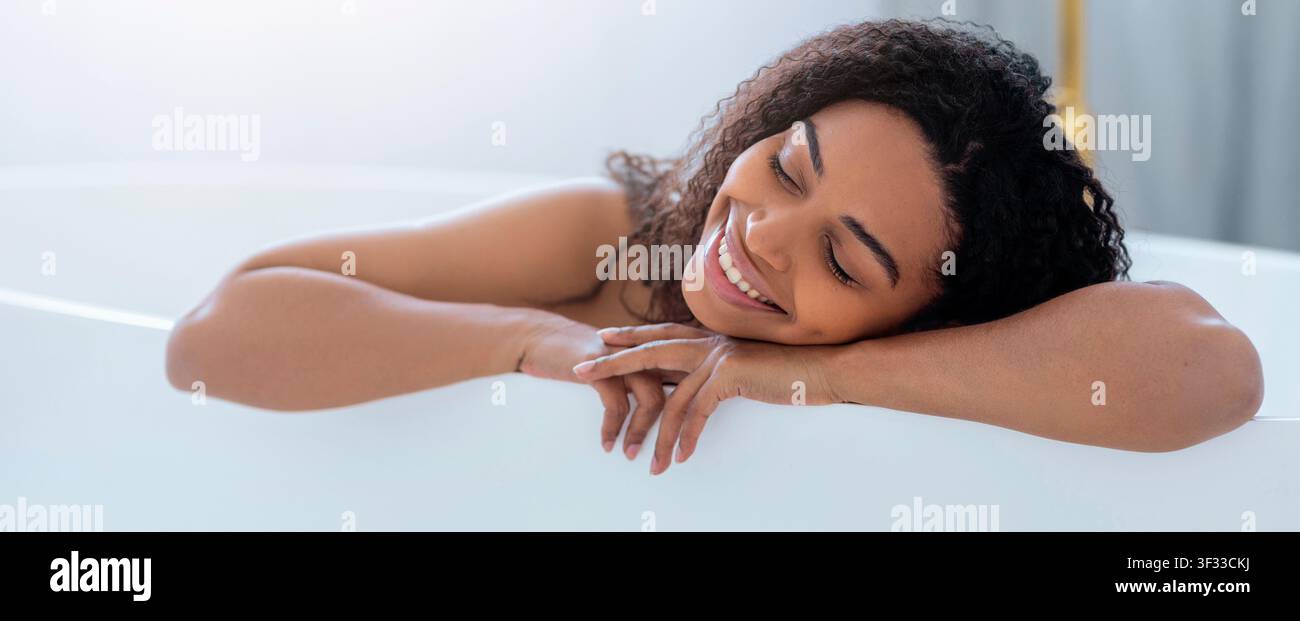 Donna nera felice che si rilassa nella vasca da bagno, godendosi un momento di pace a casa, concetto di cura di sé Foto Stock