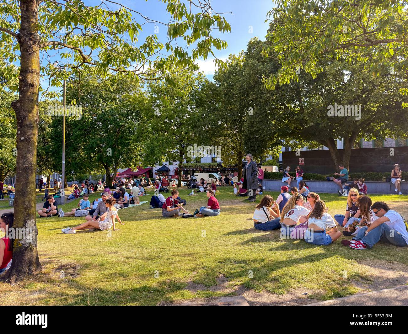 In una calda giornata estiva a Galway, in Irlanda, locali e turisti godono del sole o dell'ombra nell'Eyre Square nel centro città - Immagine stock catturata con smartphone