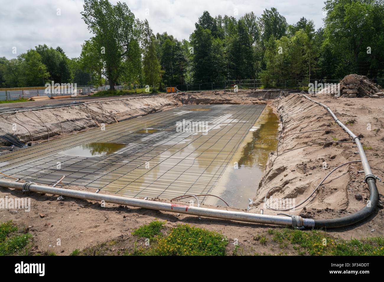 Grande lastra di fondazione in cemento armato in costruzione con reti di armatura, acqua stagnante e tubi di drenaggio in una scava Foto Stock