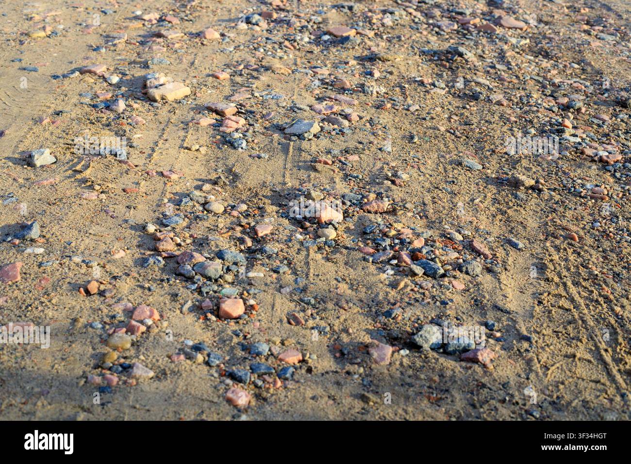 Strada rurale sabbiosa con texture di terreno ghiaioso e sabbioso. Sfondo naturale di un sentiero di terra con piccoli ciottoli di granito rosa, pietre frantumate e pista sterrata Foto Stock