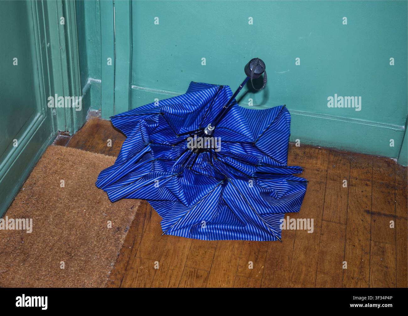Ombrello blu piegato su pavimento di legno nel corridoio di una casa dopo un temporale Foto Stock