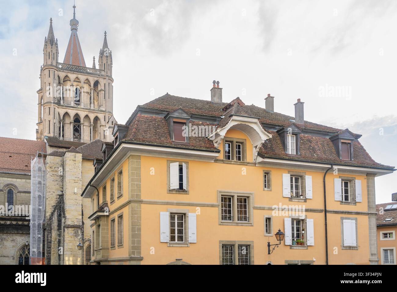 Vista della storica cattedrale di Losanna che si erge sopra un tradizionale edificio giallo con tegole di terracotta e persiane bianche a Losanna, Vaud, Sv Foto Stock