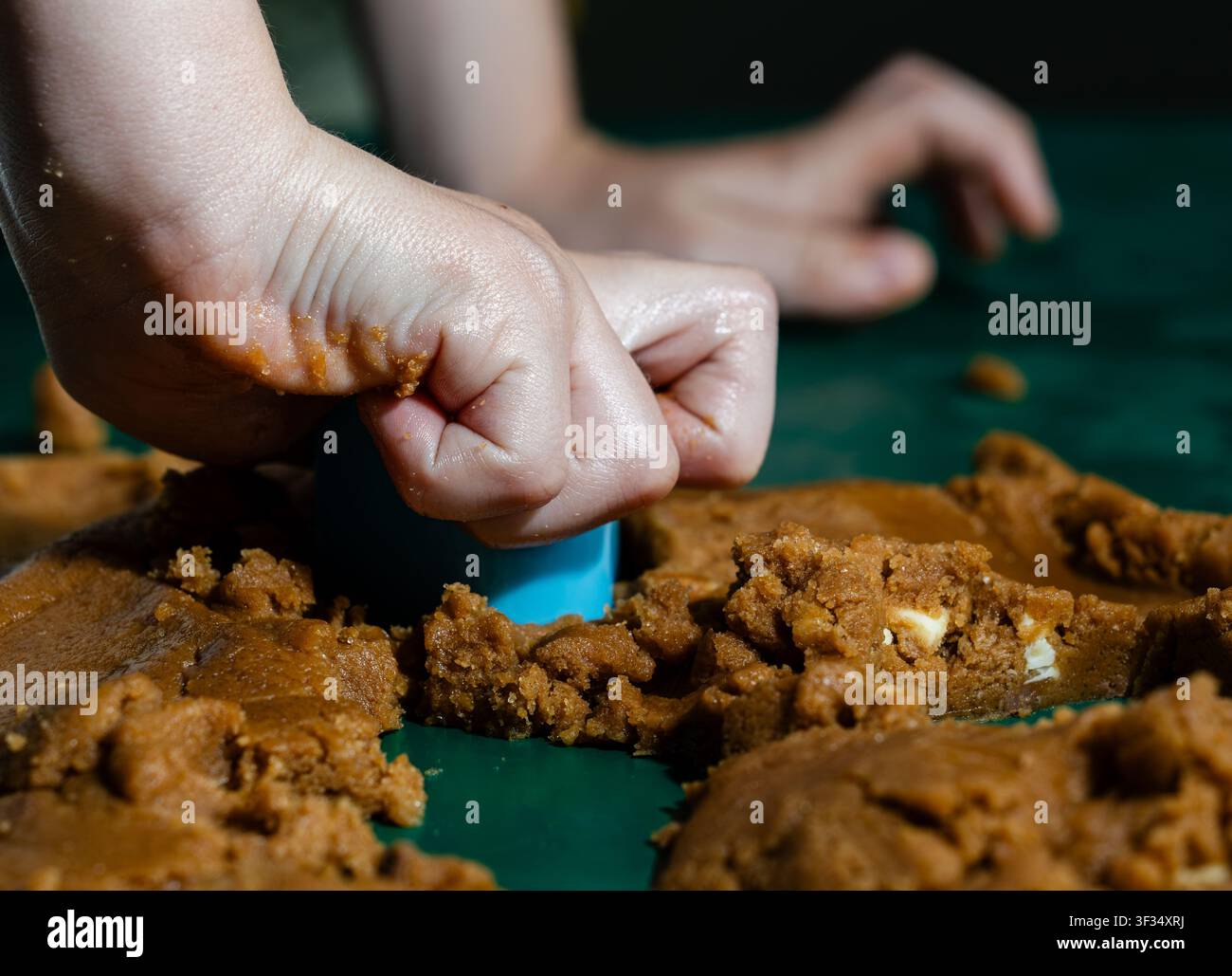 Bambino che preme uno stampino per biscotti nell'impasto di pan di zenzero durante un'attività di pasticceria casalinga Foto Stock