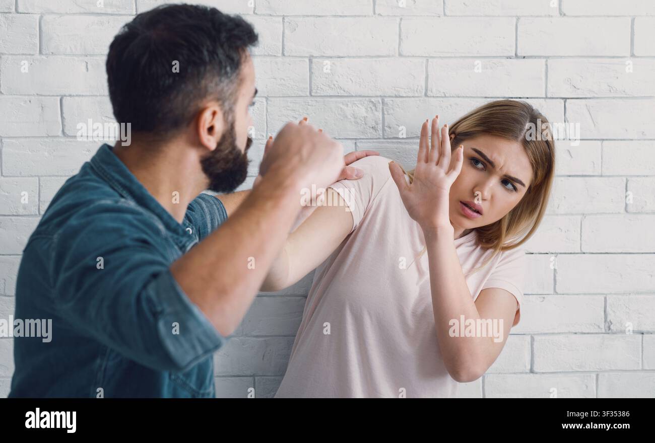 Marito batte sua moglie a casa. L'uomo arrabbiato alza il pugno a una donna spaventata Foto Stock