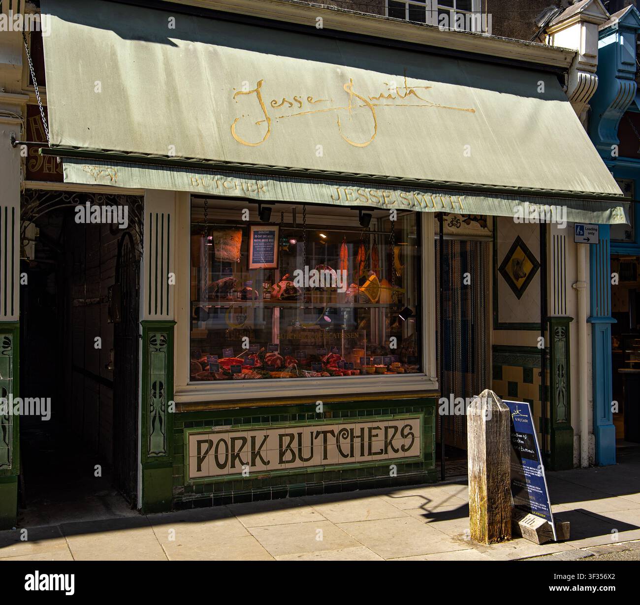 Facciata di macelleria britannica tradizionale con classico esterno in piastrelle verdi, tenda parasole e vetrina con carne a Cirencester, UK Foto Stock