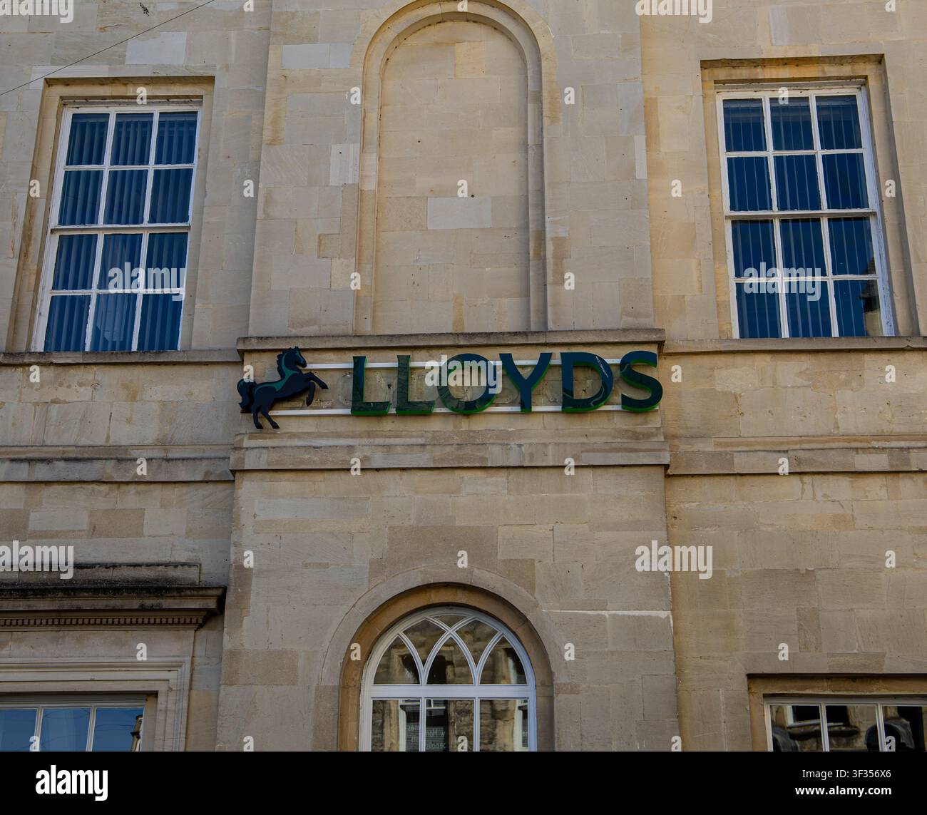 Facciata esterna di un edificio in pietra con il logo della Lloyds Bank che presenta l'iconico simbolo del cavallo nero e finestre ad arco classiche, Cirencester UK Foto Stock