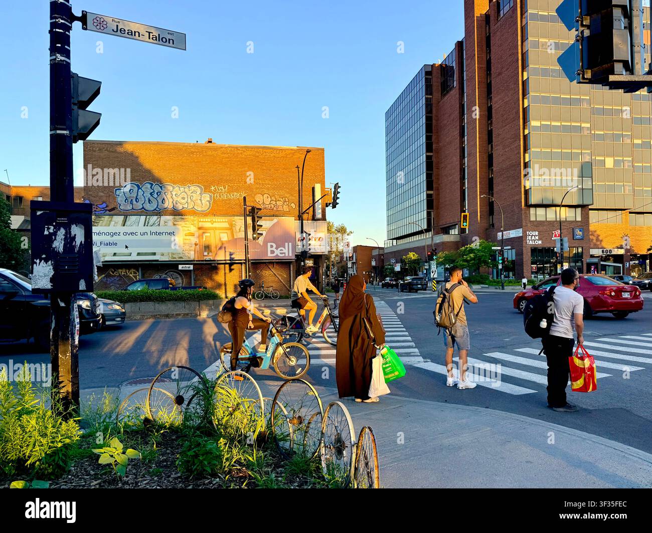 Pedoni e ciclisti multiculturali attendono a un passaggio pedonale su Jean-Talon Street a Montreal, Quebec, Canada, alla luce calda della sera Foto Stock