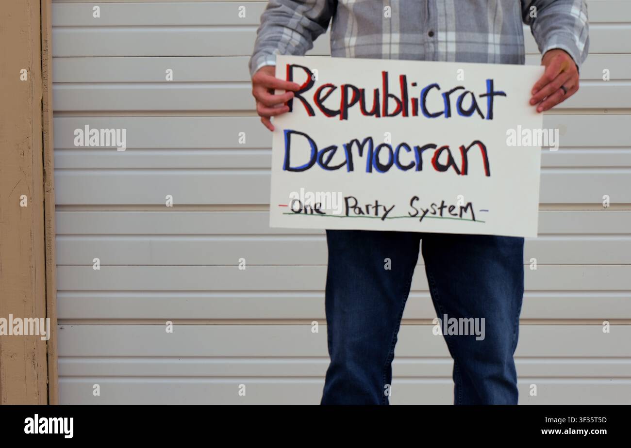 Manifestante tiene un cartello fatto a mano con la scritta "Republicrat Democran One Party System" che protesta contro l'influenza delle aziende sul duopolio politico delle elezioni e la scelta Foto Stock