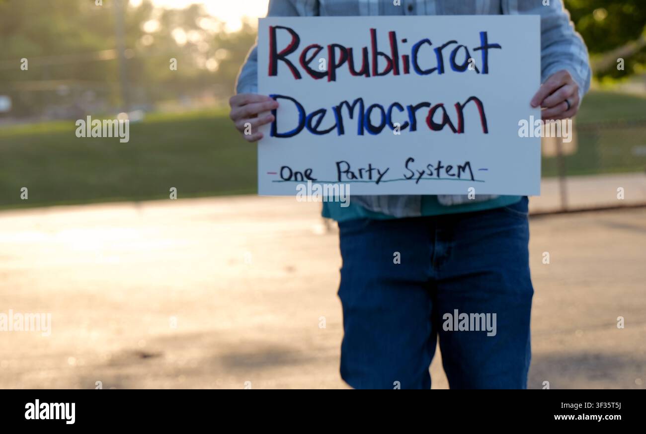 Manifestante tiene un cartello fatto a mano con la scritta "Republicrat Democran One Party System" che protesta contro l'influenza delle aziende sul duopolio politico delle elezioni e la scelta Foto Stock