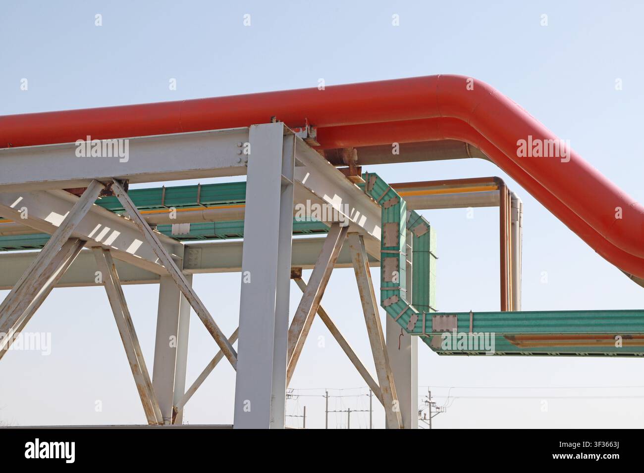 In uno stabilimento industriale, gomiti a grande raggio di tubi rossi e vassoi per cavi verdi sono disposti ordinatamente su supporti strutturali in acciaio, con linea di trasmissione Foto Stock