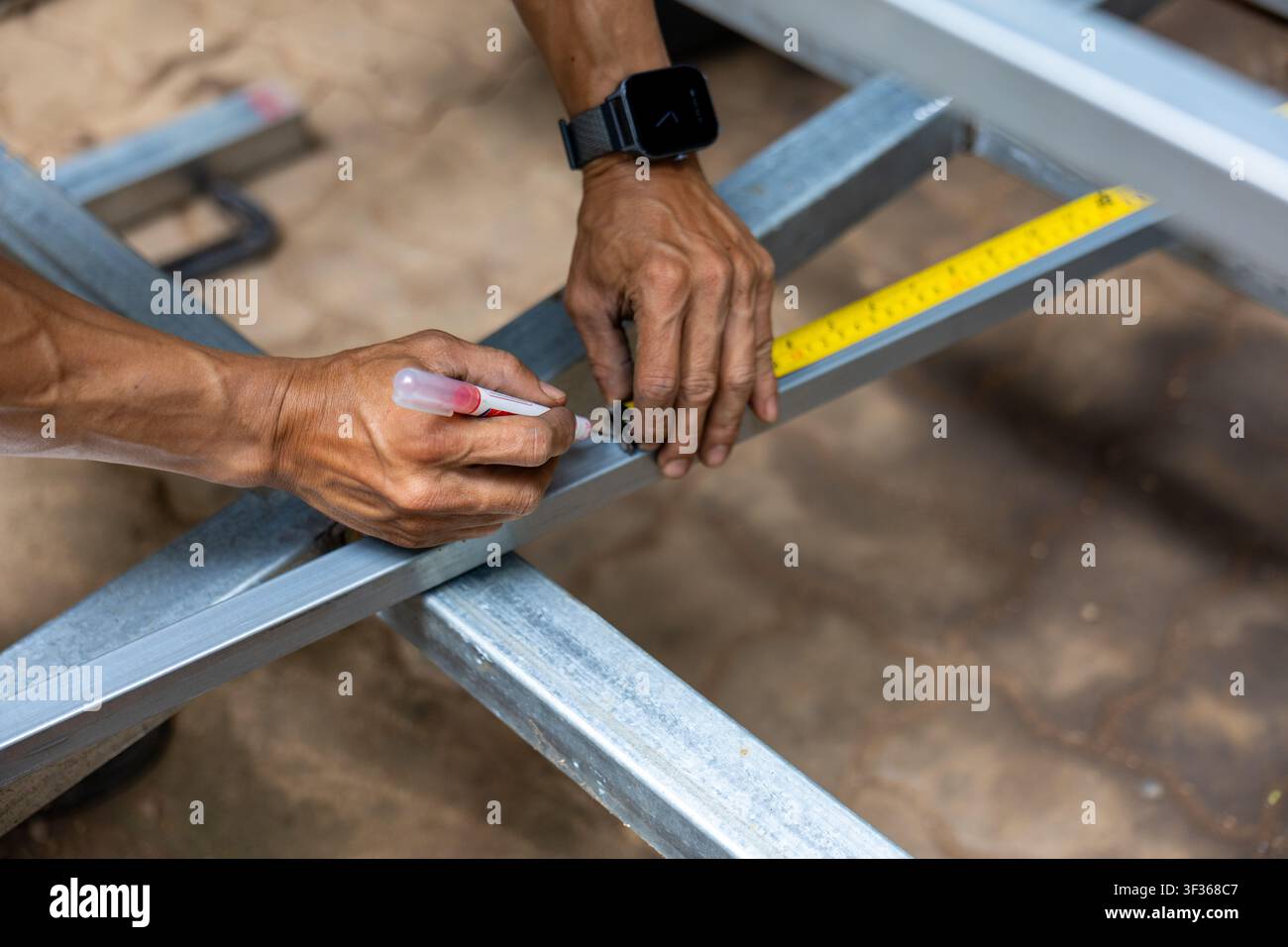 Un operaio che segna misure su una struttura metallica con un pennarello e un metro a nastro, mani concentrate che mostrano precisione e concentrazione Foto Stock
