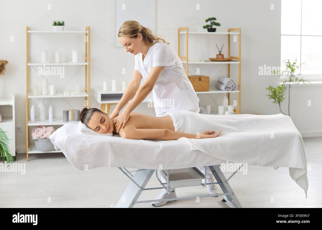 Masseur femminile che offre un massaggio rilassante alla schiena e alle spalle a una giovane cliente in un salone di spa. Foto Stock