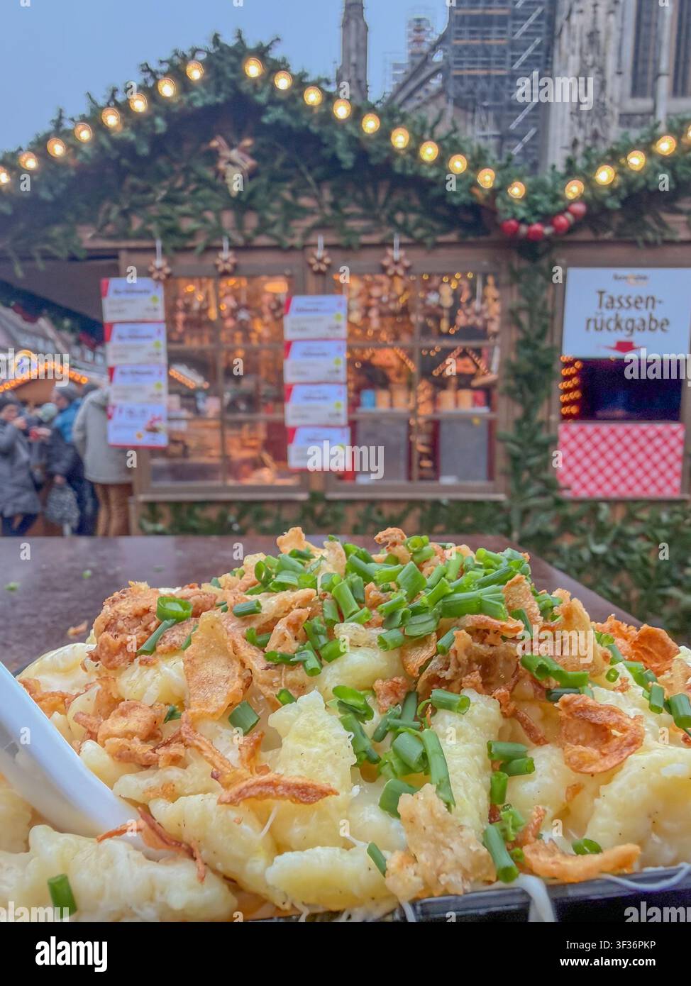 ULM, GERMANIA - 13 DICEMBRE 2025: Primo piano di tradizionali Kässpätzle svevi con cipolle fritte e erba cipollina, serviti al mercato natalizio di Ulma. Foto Stock