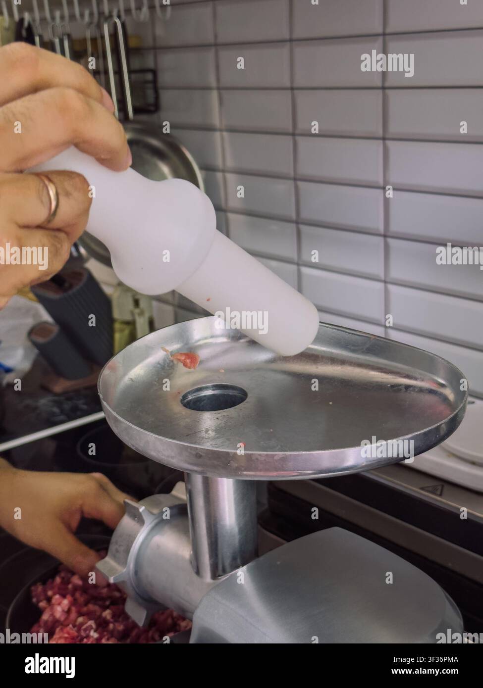 Utilizzare uno spingitore per tritacarne per premere in modo sicuro la carne cruda nel tritacarne elettrico durante la preparazione di carne macinata fatta in casa nella cucina domestica Foto Stock