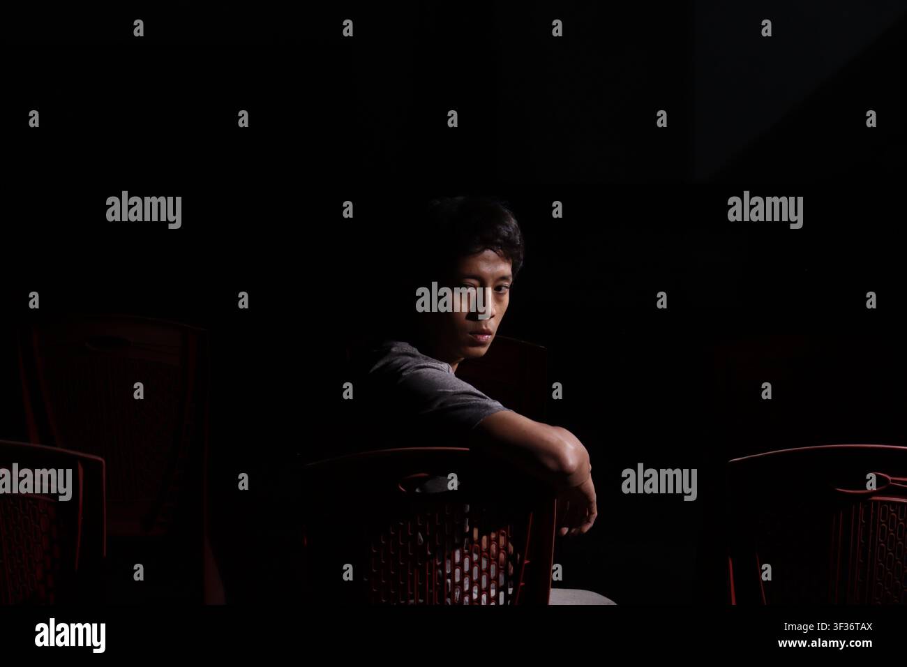Uomo che guarda nel teatro buio, scrutando le file vuote con paura come se percepisse una presenza invisibile dietro di sé. Foto Stock