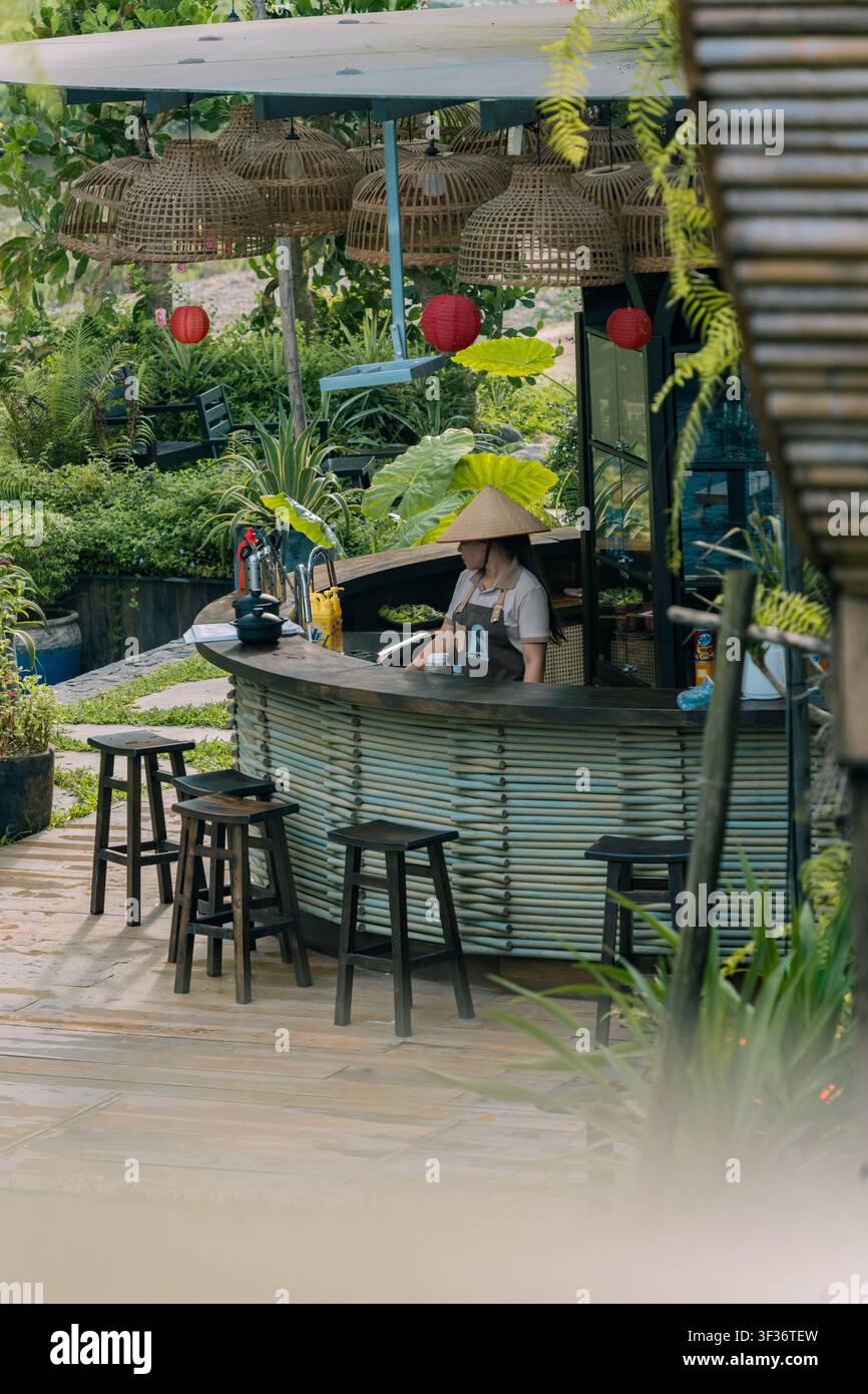 Barista che serve bevande a un bancone curvo in bambù sotto lanterne tessute, resort sul fiume di Ninh Binh, Vietnam Foto Stock