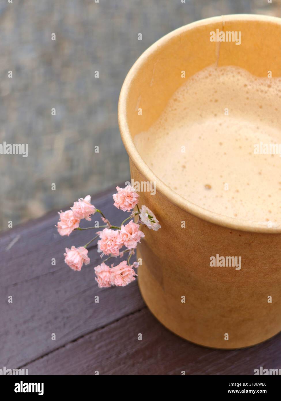 Bellissima tazza da caffè in carta artigianale con delicate fiori rosa posizionati su una panchina di legno. - Immagine stock catturata con smartphone