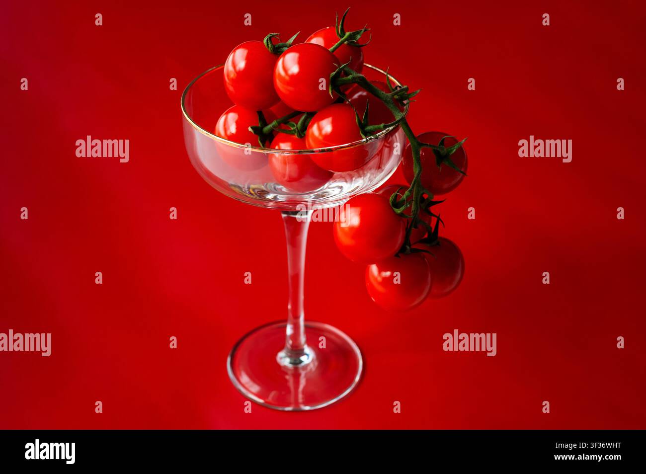 Tomate d'uva fresche in un bicchiere da cocktail su uno sfondo rosso vivace per concetti di cibo e bevande salutari. Foto Stock