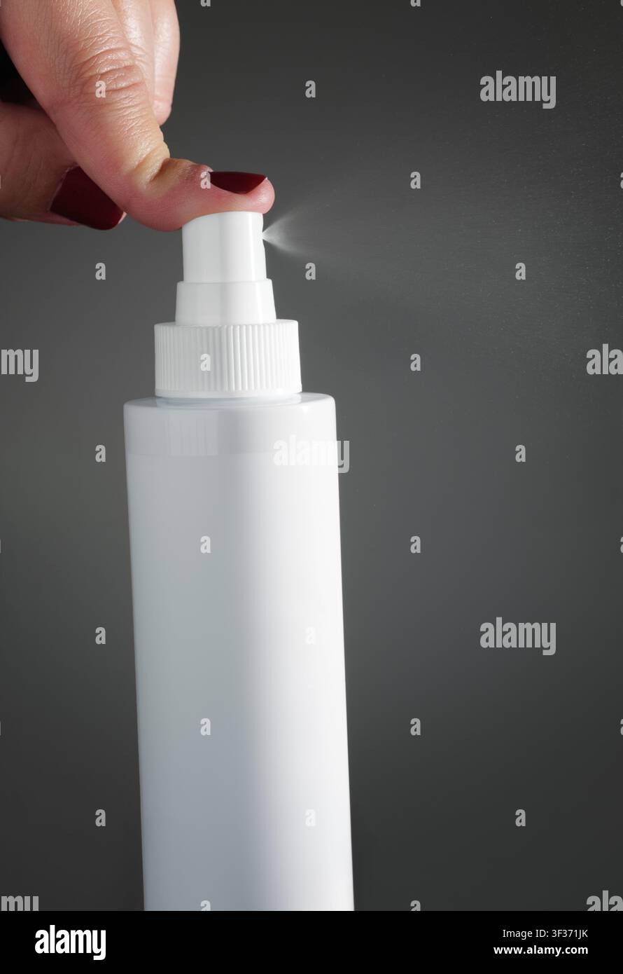 Una donna preme con il dito l'ugello di una bottiglia spray di plastica bianca vuota che spruzza nebbia su uno sfondo scuro. Foto Stock