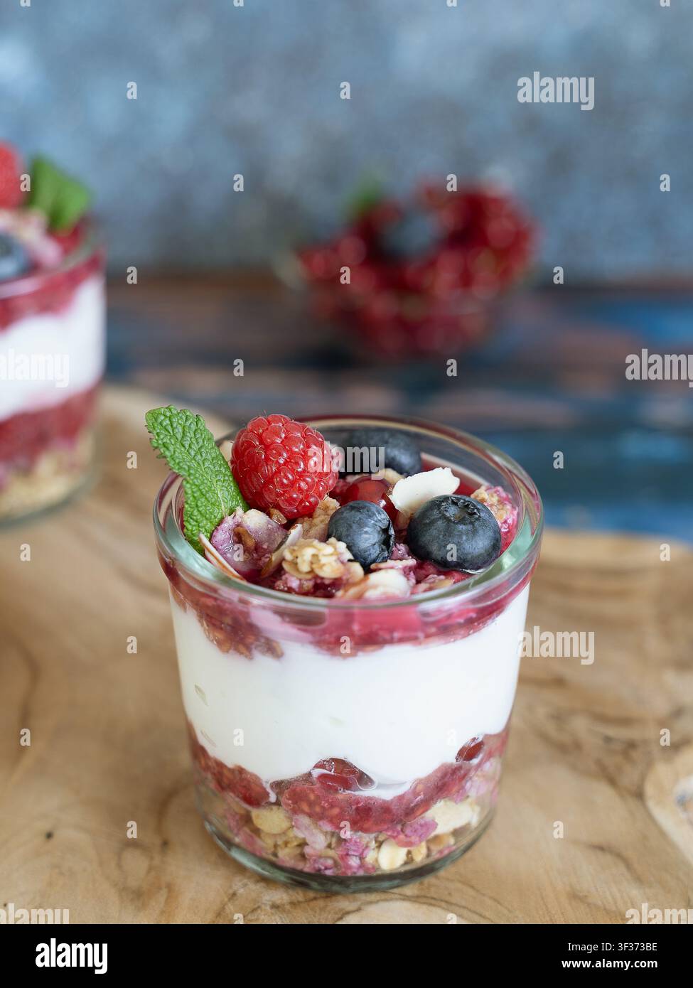 Dessert a strati con yogurt, frutti di bosco, granola e menta, presentato in un bicchiere su una superficie di legno rustico Foto Stock