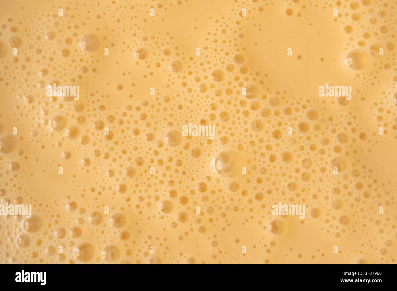Prima vista della texture di un frullato di mango. Sfondo di schiuma di frullato all'arancia, foto macro di bolle di frullato di frutta, vista dall'alto di un cocktail schiumoso e latteo montato Foto Stock