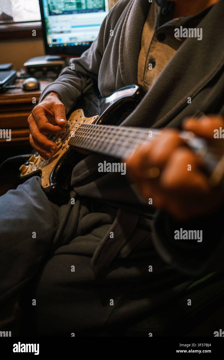 Musicista che suona la chitarra elettrica indossando una vestaglia in uno studio di musica domestico Foto Stock