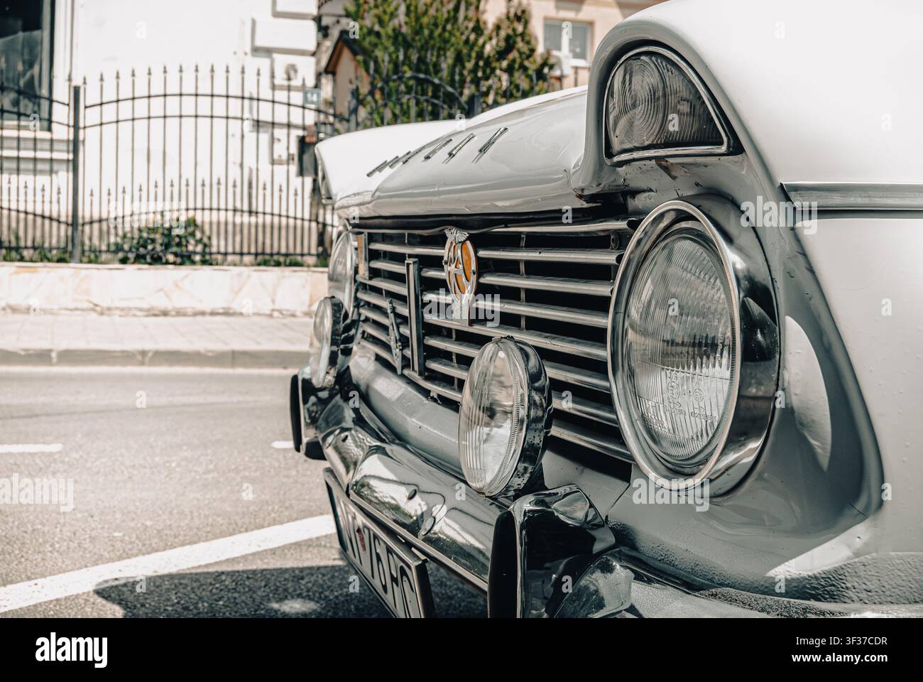 Prima di un primo piano del quarto anteriore di un'auto classica Hillman bianca con griglia cromata, fari rotondi, badge classici e uno sfondo di strada parcheggiata Foto Stock