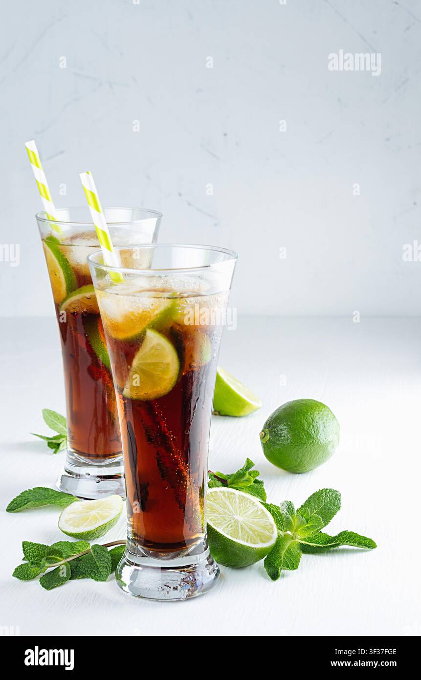Bevanda alcolica rinfrescante cuba libre con cola, ghiaccio, menta, lime, paglia in due lunghi bicchieri bagnati in una moderna cucina bianca, spazio copia. Foto Stock