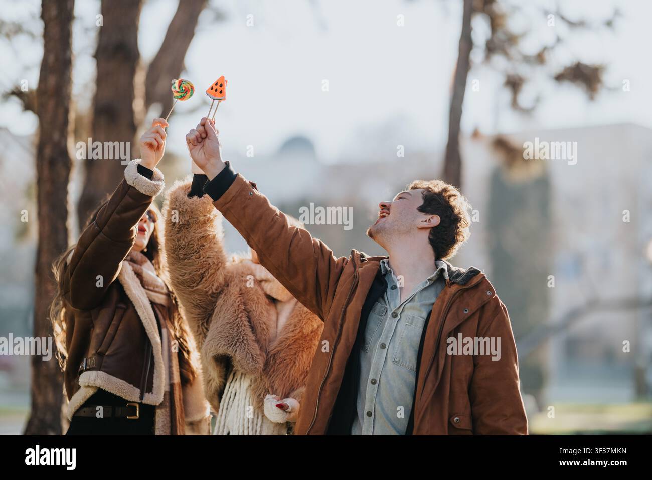 Amici casual che si divertono all'aperto condividendo lecca-lecca colorati con i cappotti invernali Foto Stock