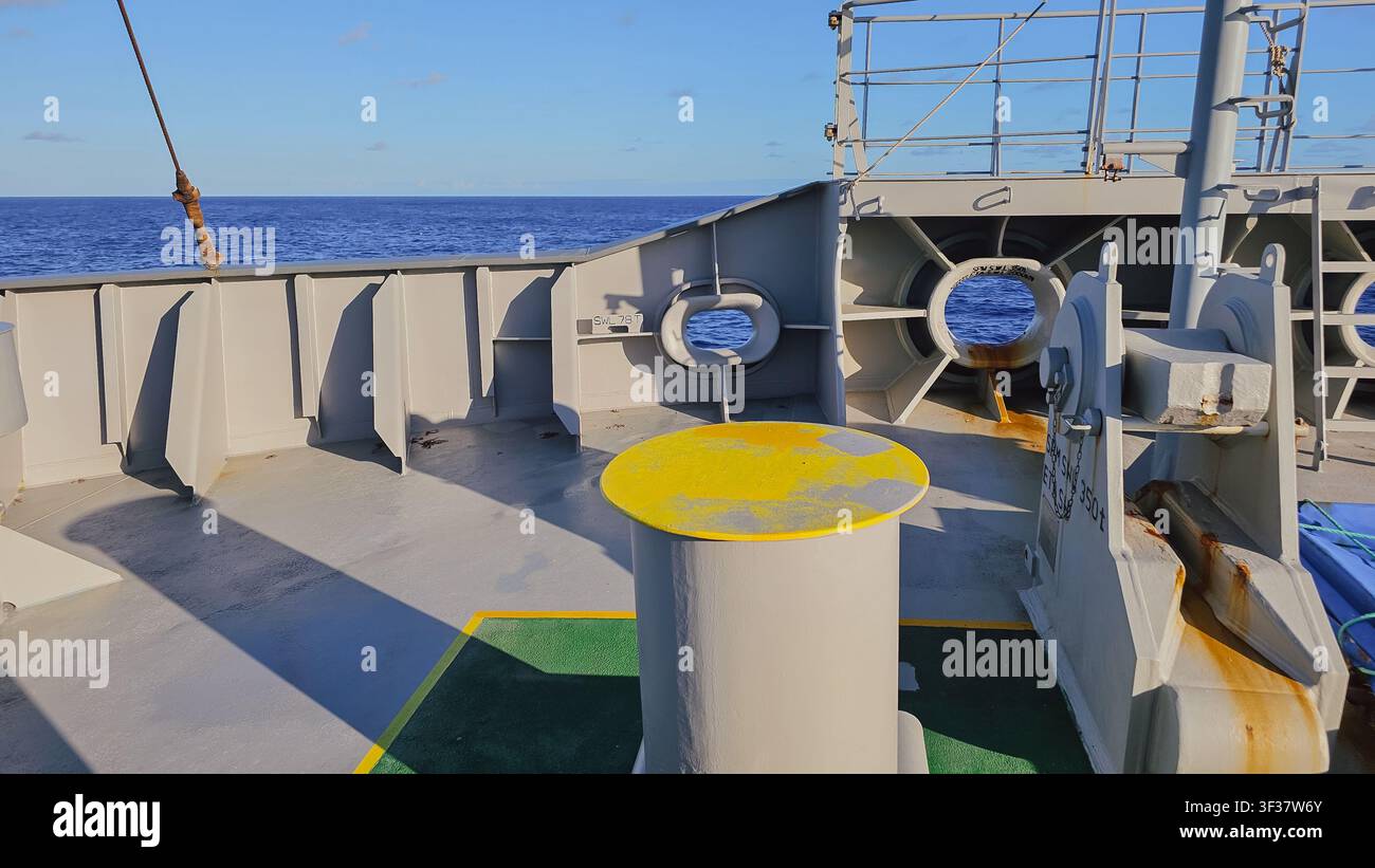 Vista ravvicinata di un bollardo di ormeggio giallo e delle calette di guida sul ponte di prua di una nave con sfondo di orizzonte oceanico blu per il trasporto marittimo Foto Stock