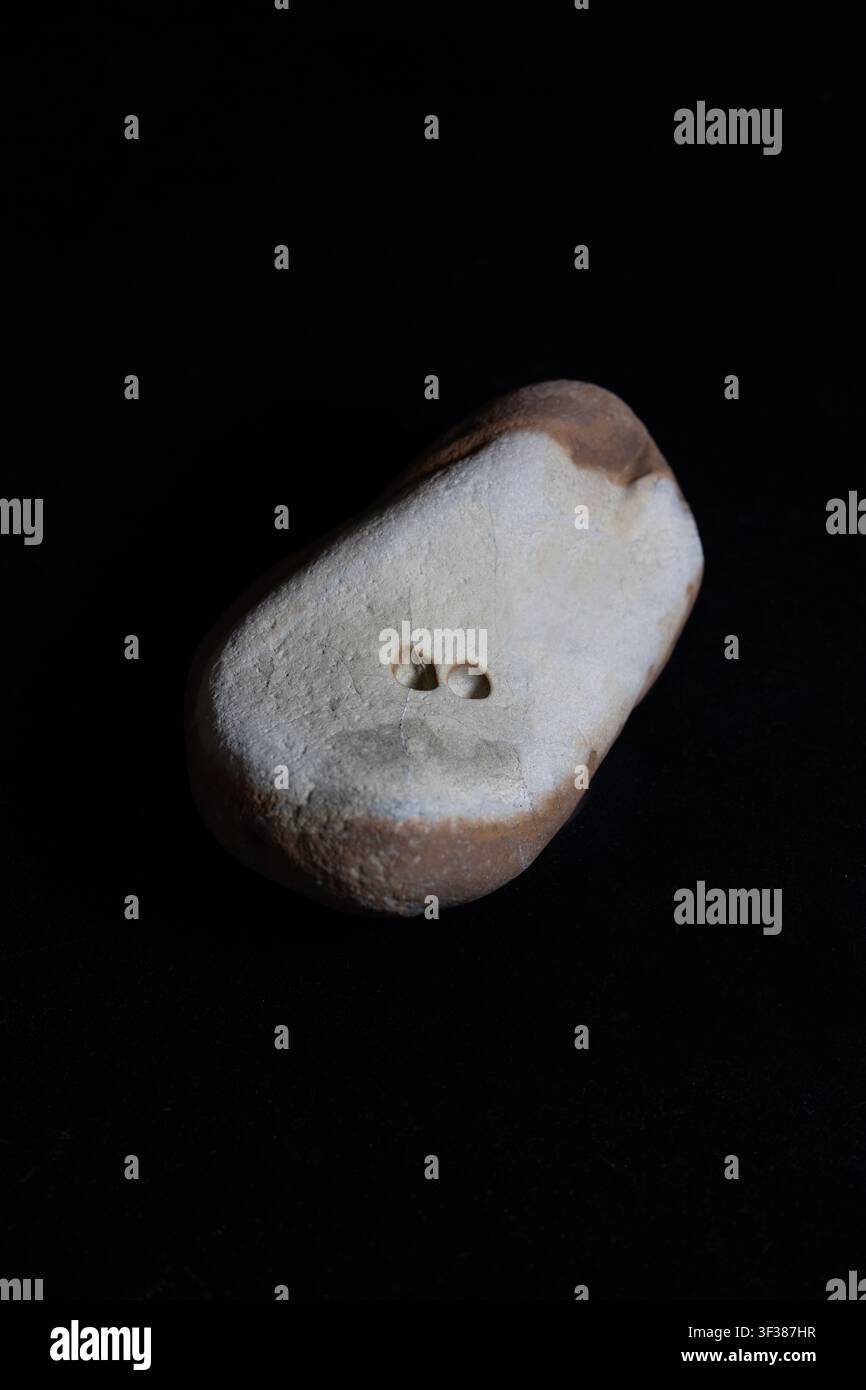 Una roccia bicolore insolita con due piccoli fori, su uno sfondo nero. Foto Stock