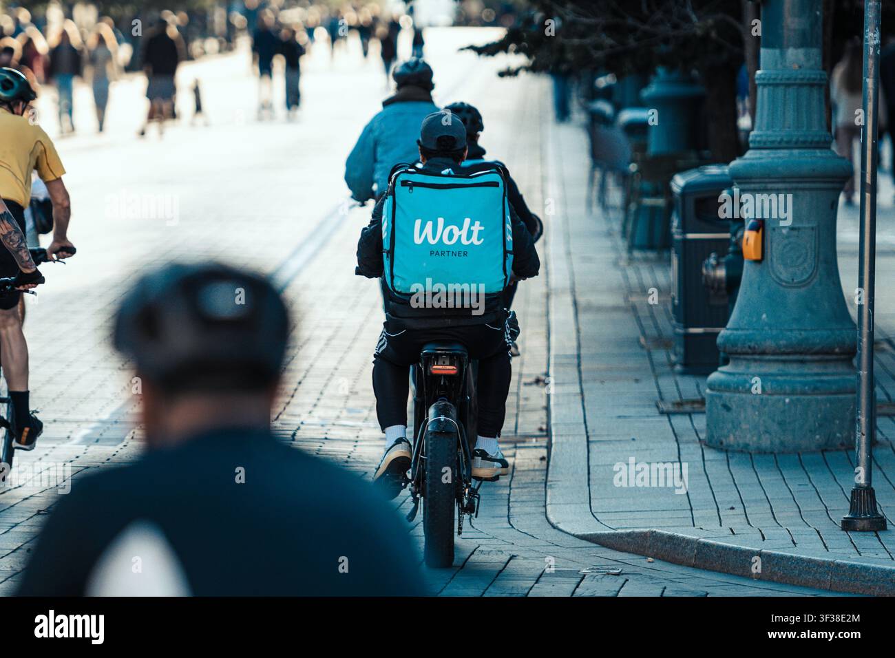 Corriere di consegna Wolt in bicicletta elettrica che trasporta oggetti in uno zaino blu chiaro del marchio Foto Stock