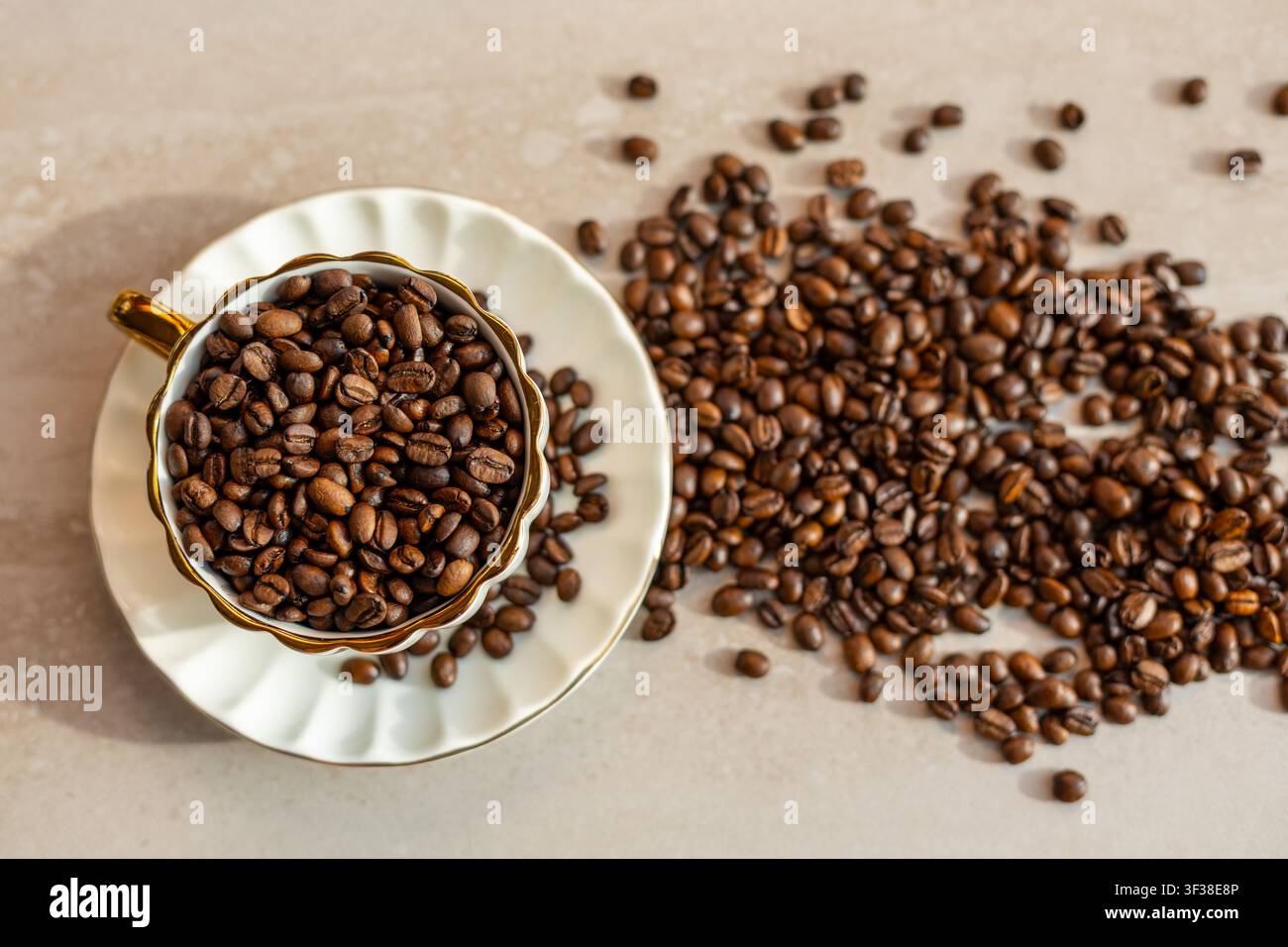 Caffè tostato in tazza e piattino decorativi. Vista dall'alto di chicchi di caffè tostati che riempiono una tazza bianca decorativa e sparsi su un beige Foto Stock