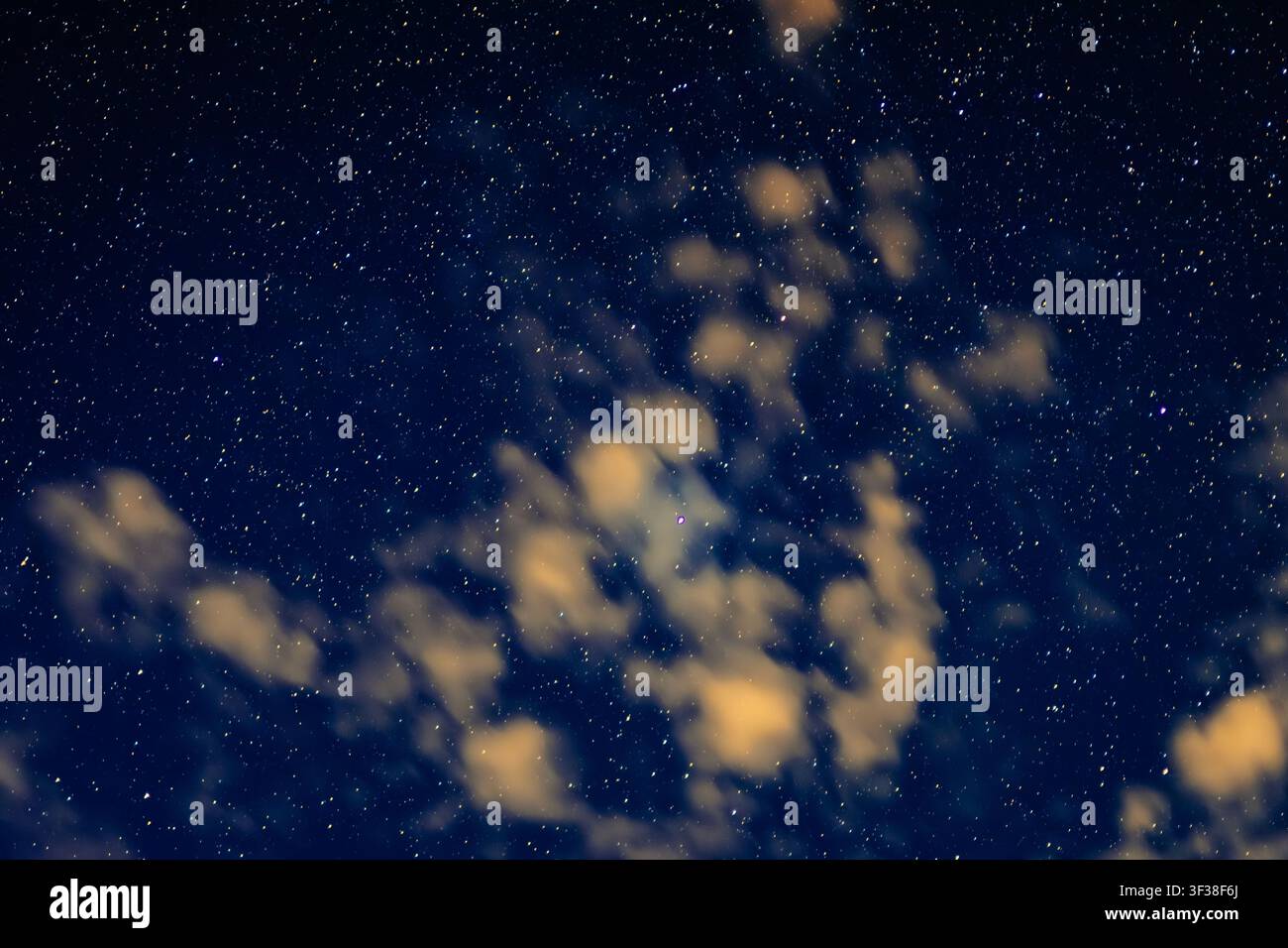 Fotografia astrofotografica grandangolare che cattura un cielo notturno stellato pieno di un campo denso di stelle brillanti, magnificamente interrotto da nuvole sparse Foto Stock