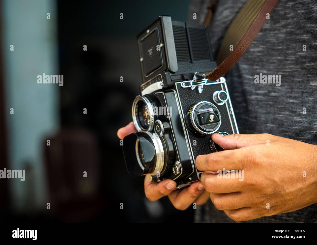 Primo piano di una persona che tiene una fotocamera reflex a doppia lente vintage con controlli manuali e una cinghia di cuoio, evidenziando la classica fotocamera fotografica. Foto Stock