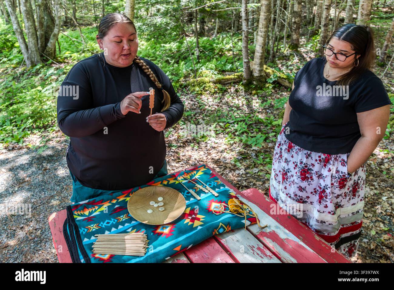 Un facilitatore culturale mostra a un partecipante i pezzi di gioco per il tradizionale gioco di dadi Mi’kmaq, Waltes, a un tavolo da picnic sul sentiero di Goat Island nella Prima Nazione di Eskasoni, Nuova Scozia, Canada. Nel gioco, sei dischi dipinti su entrambi i lati vengono lanciati da una ciotola di legno e i punti vengono conteggiati utilizzando dei bastoncini Foto Stock
