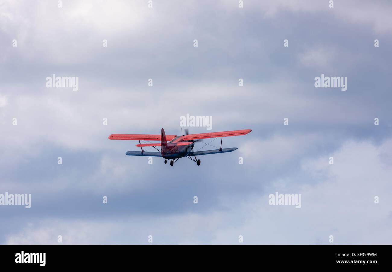 Borne Sulinowo, Polonia – 13 agosto 2023: Biplano rosso che si eleva nel cielo nuvoloso, le ali lo portano più in alto Foto Stock