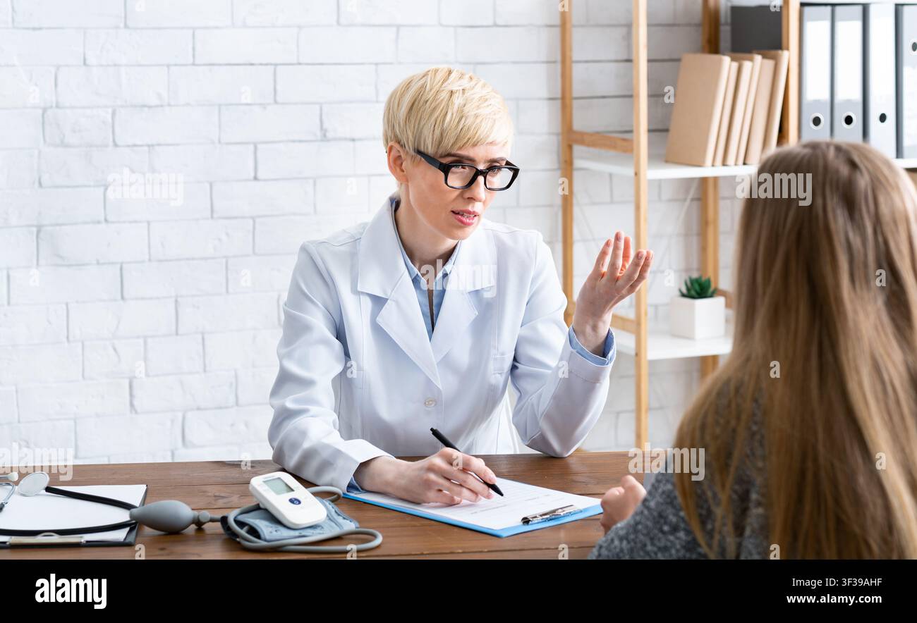 Consigli del medico. Donna in occhiali e cappotto bianco, consiglia paziente Foto Stock