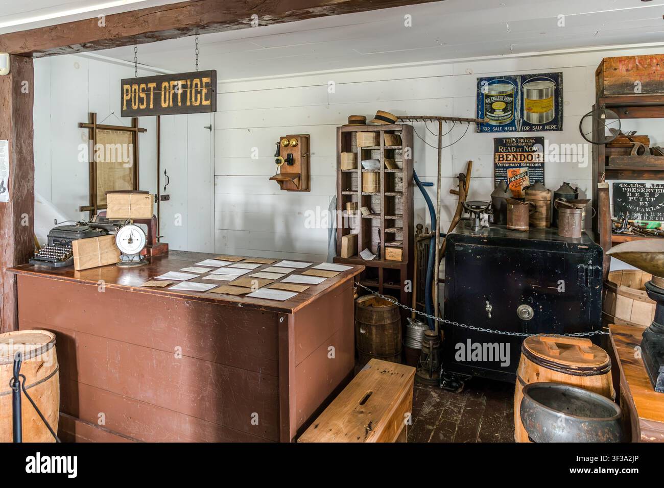 L'angolo della posta nel negozio generale A.M. McLeod presso l'Highland Village Museum | Baile nan Gàidheal a Iona, Nuova Scozia, Canada, presenta una macchina da scrivere meccanica, una bilancia postale e una cassaforte in acciaio nero. Sul muro è appeso un manifesto pubblicitario per il medicinale veterinario ‚Bendor‘ Foto Stock