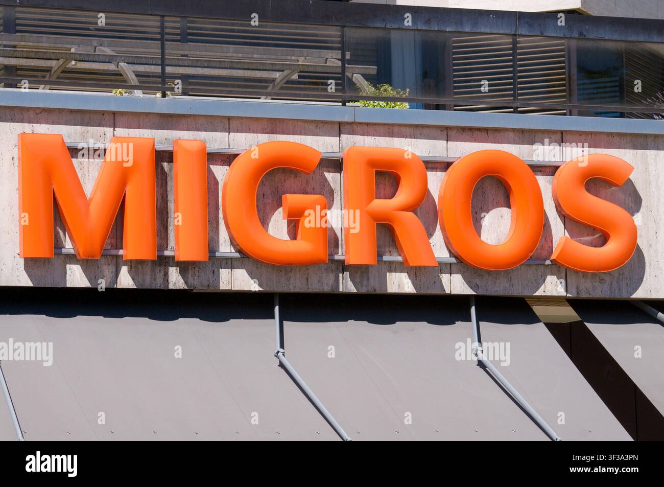 Lugano, Ticino, Svizzera - 11 giugno 2026: Insegna iconica 3D arancione del supermercato Migros montata sulla facciata di un negozio. Foto Stock
